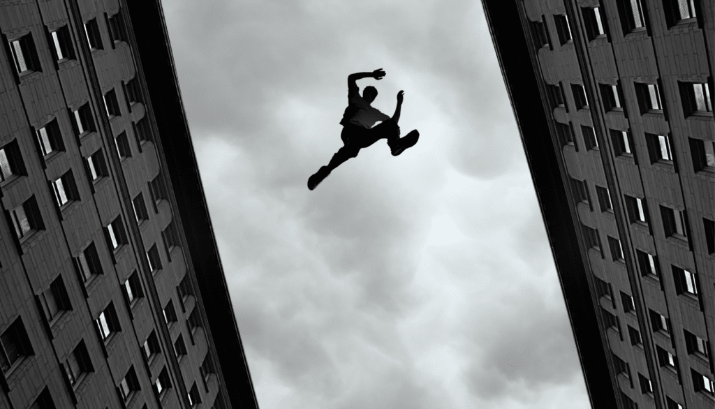 Person jumping from one building rooftop to another, grey-toned image