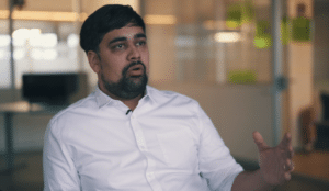 Amit looking right, wearing white buttoned shirt, blurry office background