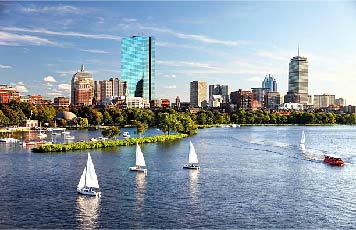 Boston city buildings with greenery and water foreground and white boats