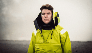 Adrian Bleninger sailor in bright neon coat against wrm grey background